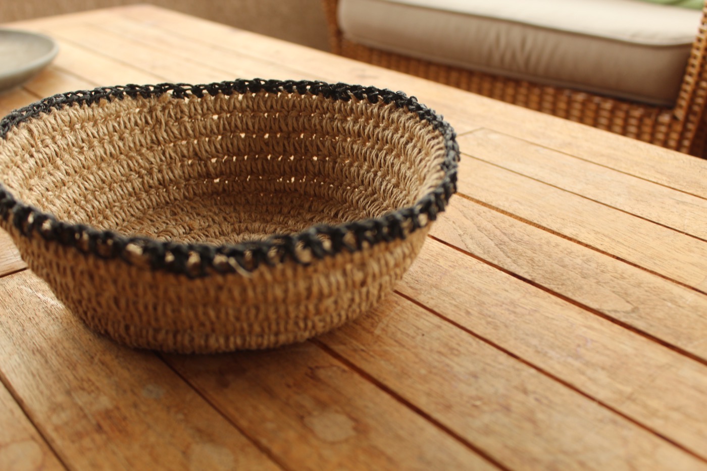 Canasto de yute con borde tejido en negro sobre una mesa de madera