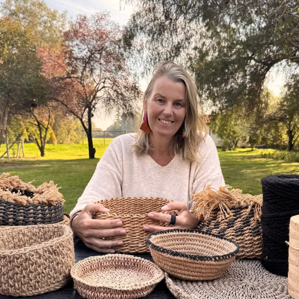 Julie, fundadora de Aire Puro, sentada en el jardín con sus canastos de yute tejidos a mano